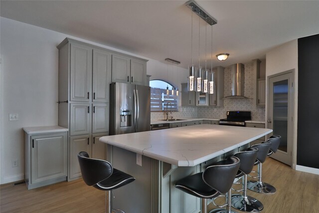 kitchen with sink, stainless steel fridge, a kitchen breakfast bar, a center island, and wall chimney range hood