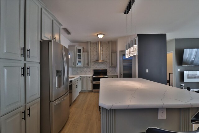 kitchen with wall chimney exhaust hood, light stone counters, tasteful backsplash, hanging light fixtures, and stainless steel appliances