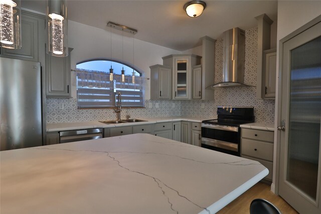 kitchen featuring gray cabinets, appliances with stainless steel finishes, decorative light fixtures, sink, and wall chimney exhaust hood