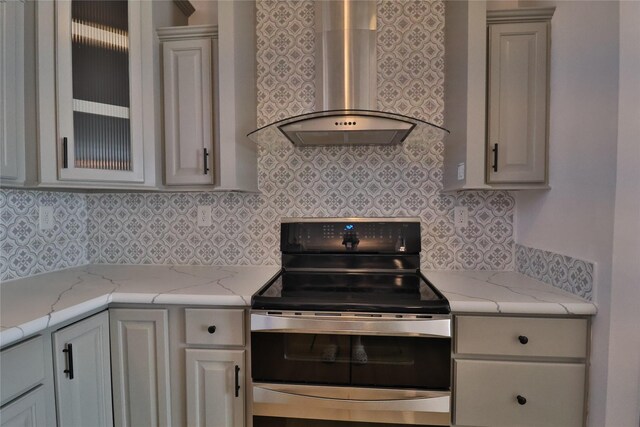 kitchen with light stone countertops, electric stove, backsplash, and wall chimney exhaust hood