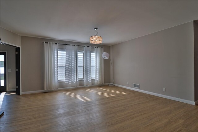 unfurnished room with hardwood / wood-style flooring, a wall mounted air conditioner, and a notable chandelier