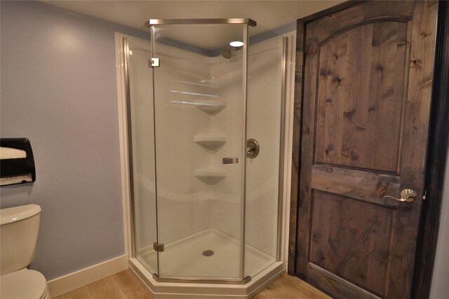 bathroom with hardwood / wood-style flooring, toilet, and a shower with door