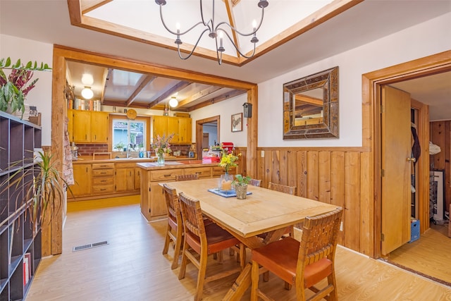 dining space with light hardwood / wood-style floors, sink, beam ceiling, and a chandelier