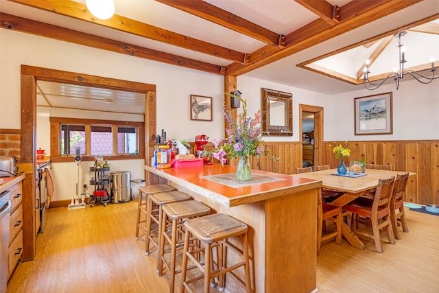 kitchen featuring light hardwood / wood-style floors, a notable chandelier, beam ceiling, and a breakfast bar