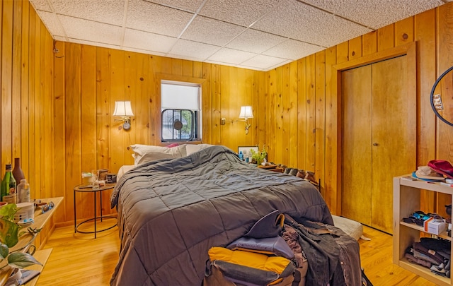 bedroom featuring a paneled ceiling, a closet, light wood-type flooring, and wooden walls