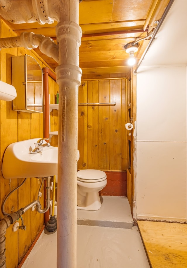 bathroom with wood walls, toilet, and concrete flooring