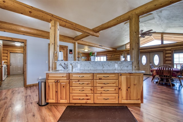 kitchen featuring log walls, a sink, light wood-style flooring, and lofted ceiling with beams