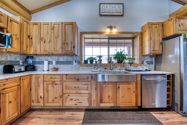 kitchen with lofted ceiling, a sink, stainless steel appliances, light wood-style floors, and backsplash