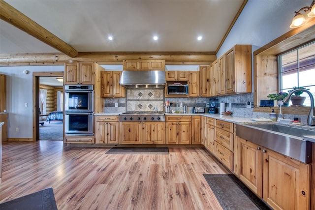 kitchen featuring vaulted ceiling with beams, log walls, stainless steel appliances, under cabinet range hood, and a sink