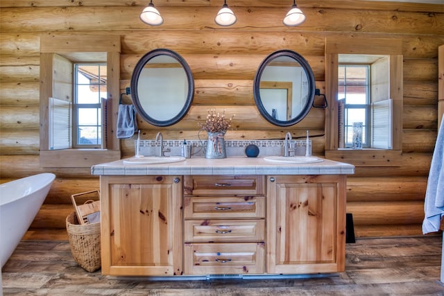 full bathroom featuring double vanity, a soaking tub, a sink, and wood finished floors