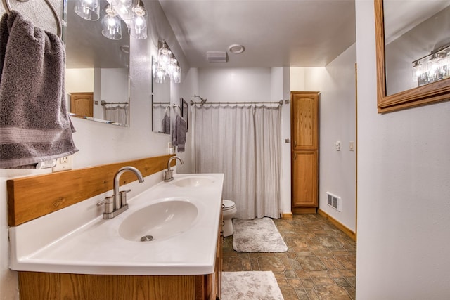 bathroom with stone finish floor, double vanity, visible vents, and a sink