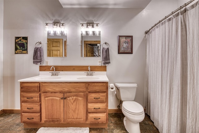 bathroom with toilet, a sink, stone tile floors, and double vanity