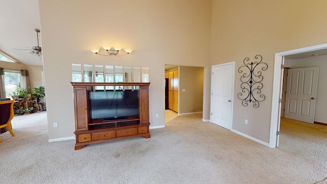 unfurnished living room with ceiling fan, a towering ceiling, and light carpet