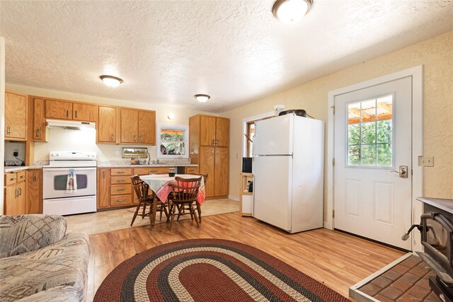 kitchen with a wood stove, a textured ceiling, light tile patterned floors, and white appliances