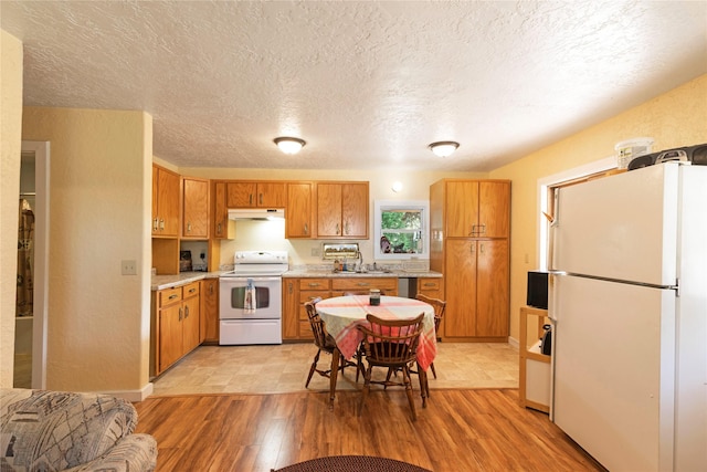 1776 Willow Creek Rd, Corvallis, MT 59828 - kitchen with white appliances, under cabinet range hood, light countertops, brown cabinets, and a textured ceiling