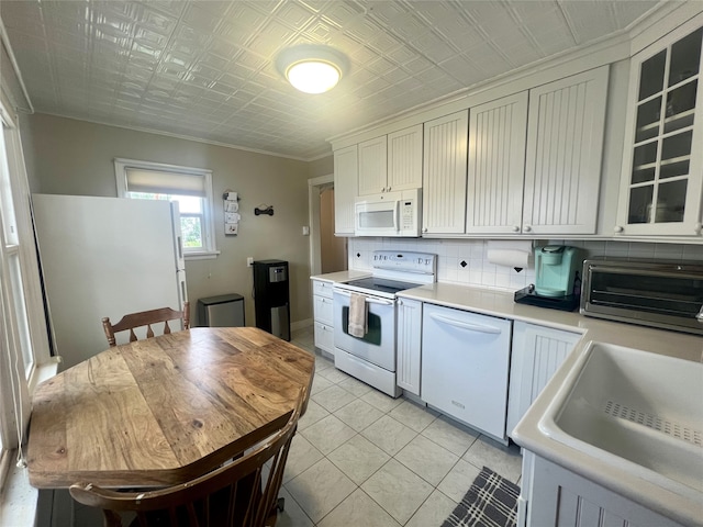 kitchen with tasteful backsplash, white appliances, sink, light tile patterned flooring, and white cabinetry