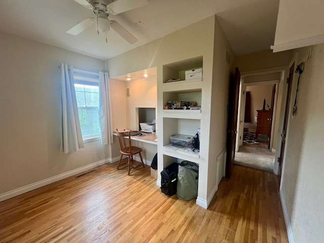 home office with built in features, ceiling fan, and light hardwood / wood-style flooring