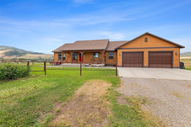 single story home with a rural view, a mountain view, a garage, and a front yard