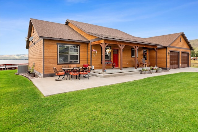 rear view of property with cooling unit, a garage, a patio area, and a lawn