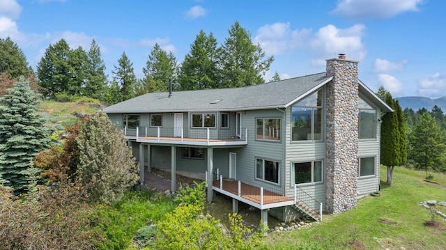 back of house with a deck with mountain view, stairway, a lawn, and a chimney