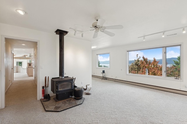 carpeted living room with baseboard heating, a mountain view, ceiling fan, and a wood stove