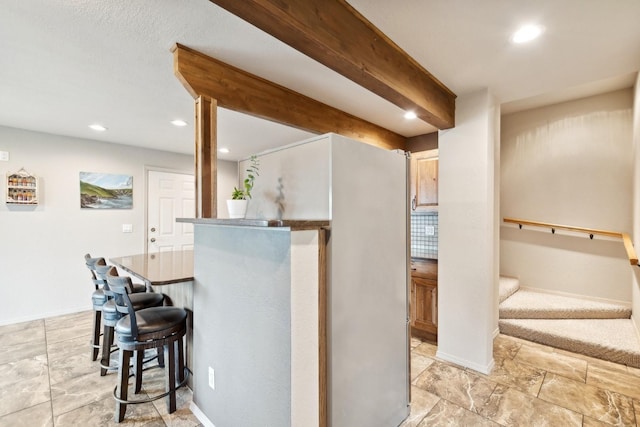 kitchen featuring a kitchen bar, beam ceiling, and decorative backsplash