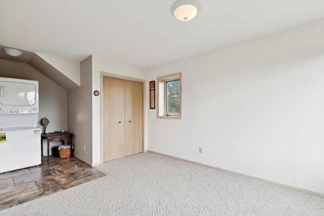 unfurnished bedroom featuring stacked washing maching and dryer, baseboards, a closet, and carpet flooring