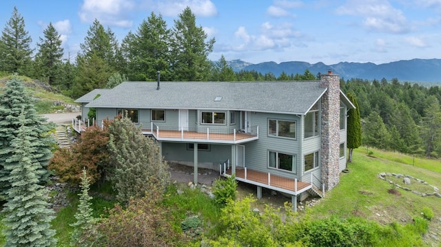 253 Pine Needle Ln, Bigfork, MT 59911 - rear view of house with a chimney, a mountain view, a balcony, a lawn, and roof with shingles