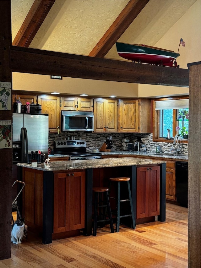 2378 Lake Creek Rd, Troy, MT 59935 - kitchen featuring appliances with stainless steel finishes, light wood-style floors, decorative backsplash, dark stone countertops, and brown cabinetry