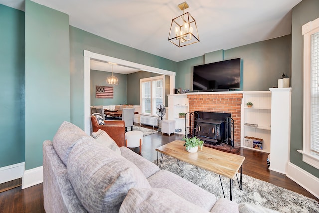 living room featuring a wood stove, a brick fireplace, radiator heating unit, dark hardwood / wood-style flooring, and a notable chandelier