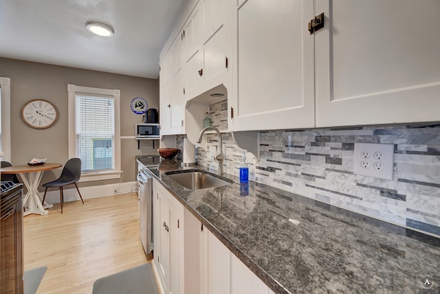 kitchen featuring dark stone countertops, light wood-type flooring, white cabinets, backsplash, and sink