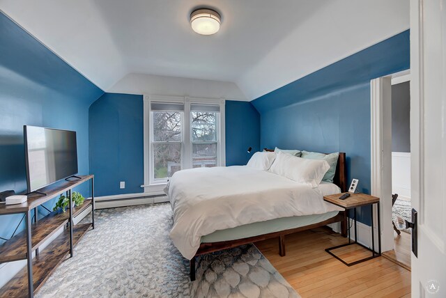 bedroom with a baseboard heating unit, lofted ceiling, and light hardwood / wood-style floors