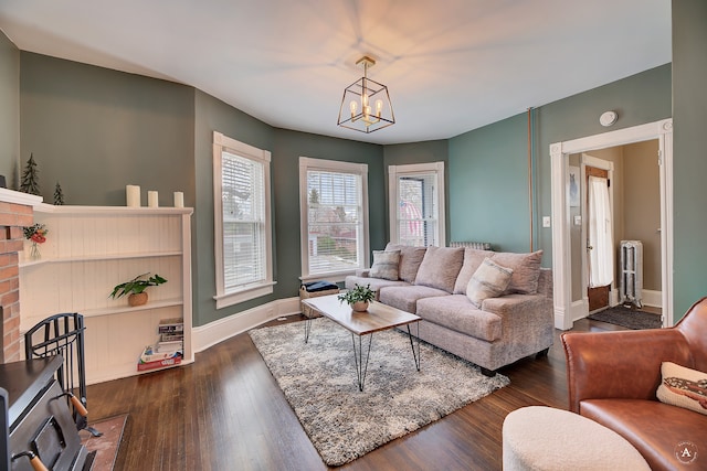 living room featuring a notable chandelier, radiator, a brick fireplace, and dark hardwood / wood-style floors