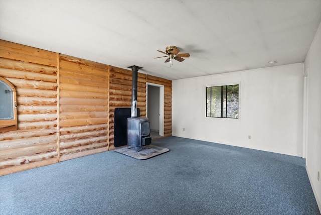 unfurnished living room with carpet, rustic walls, a wood stove, and ceiling fan