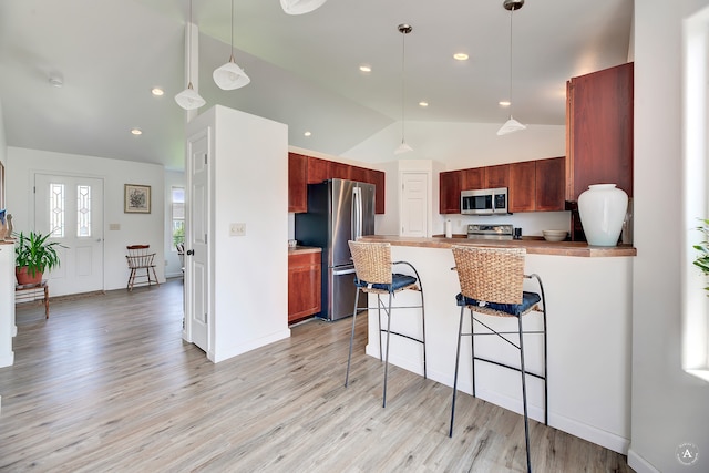 kitchen featuring appliances with stainless steel finishes, decorative light fixtures, a kitchen bar, light hardwood / wood-style floors, and kitchen peninsula