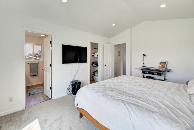 bedroom featuring ensuite bath, lofted ceiling, carpet floors, and a walk in closet