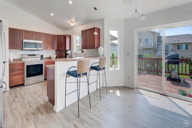 kitchen featuring light wood-type flooring, stainless steel appliances, a breakfast bar, kitchen peninsula, and hanging light fixtures