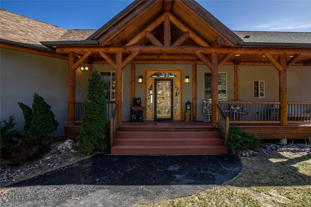 doorway to property featuring a porch, roof with shingles, and stucco siding