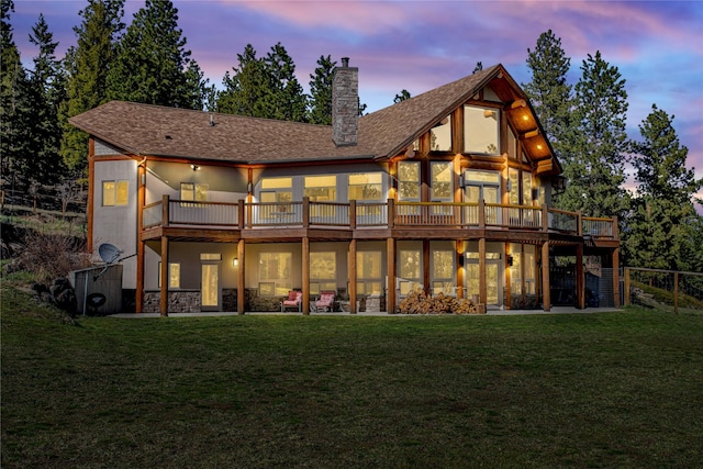 back of property at dusk with a deck, a yard, a chimney, and a shingled roof