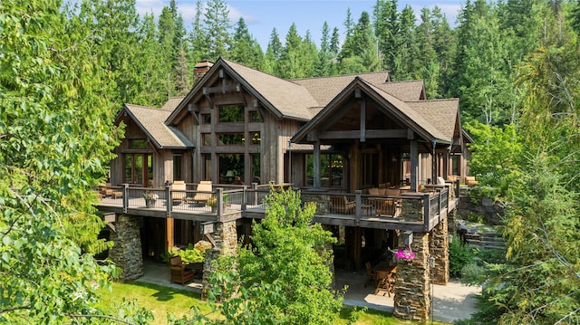 back of house featuring a wooden deck, a chimney, a shingled roof, and a patio