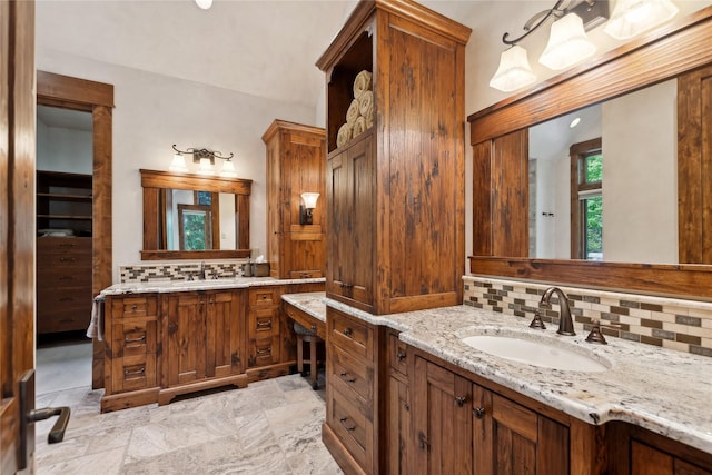 bathroom featuring stone finish flooring, backsplash, two vanities, and a sink