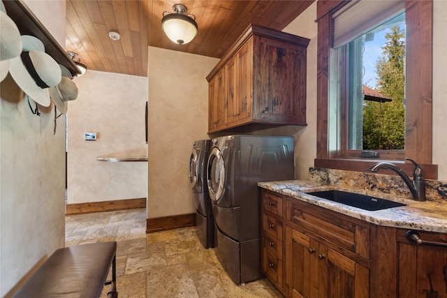 laundry area with washing machine and clothes dryer, stone tile floors, cabinet space, a sink, and wooden ceiling