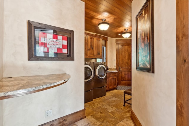 clothes washing area featuring wooden ceiling, cabinet space, washer and clothes dryer, and baseboards