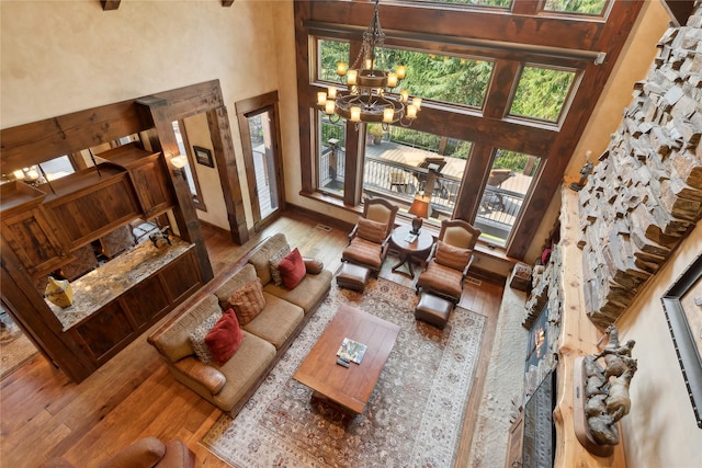 living room featuring wood-type flooring, a towering ceiling, baseboards, and an inviting chandelier