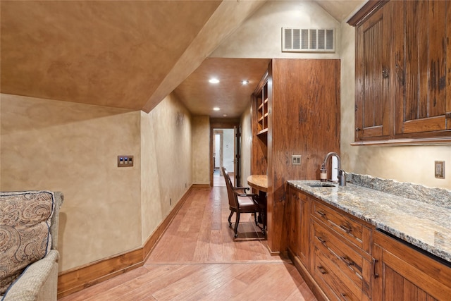 kitchen featuring light stone counters, a sink, visible vents, brown cabinets, and light wood finished floors