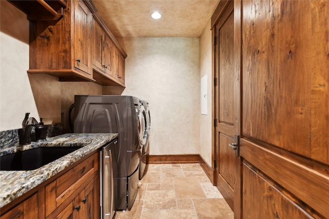 laundry room featuring separate washer and dryer, a sink, baseboards, cabinet space, and stone tile flooring