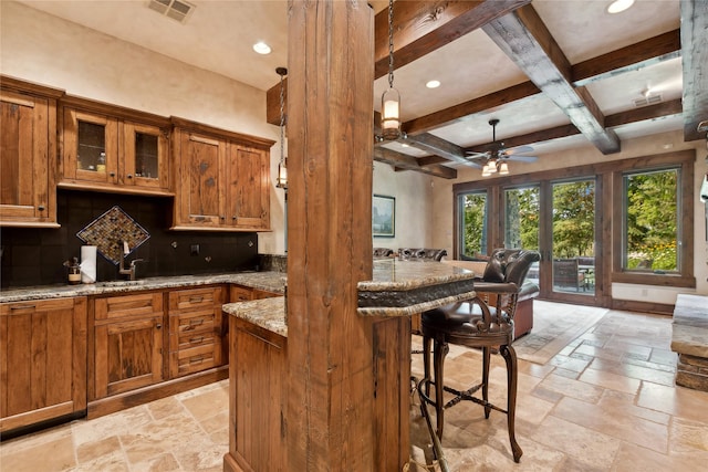 kitchen featuring brown cabinetry, coffered ceiling, a breakfast bar area, and stone tile flooring