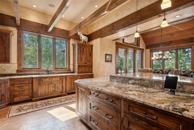 kitchen featuring light stone counters, a wealth of natural light, a sink, and hanging light fixtures