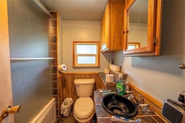 full bath with toilet, bath / shower combo with glass door, a sink, and wainscoting