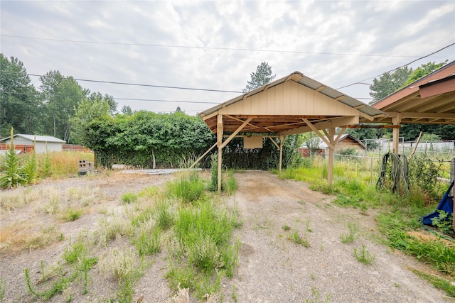 view of vehicle parking featuring dirt driveway, fence, and a detached carport